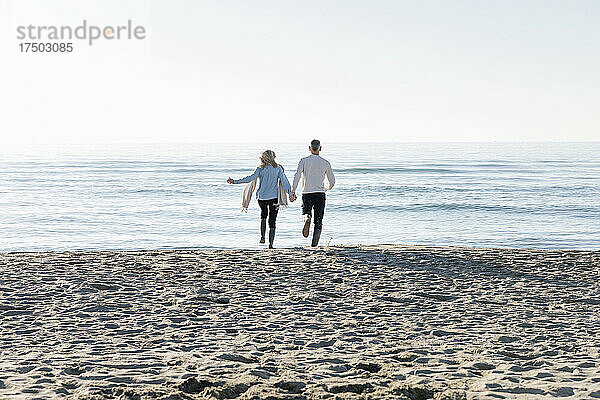 Mann und Frau rennen am Strand in Richtung Meer