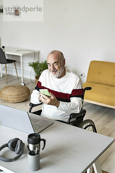 Leitender Geschäftsmann im Rollstuhl nutzt Mobiltelefon im Heimbüro