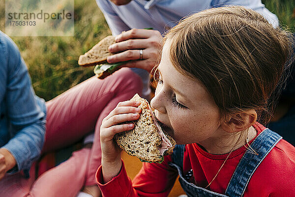 Mädchen isst Sandwich mit Eltern im Park