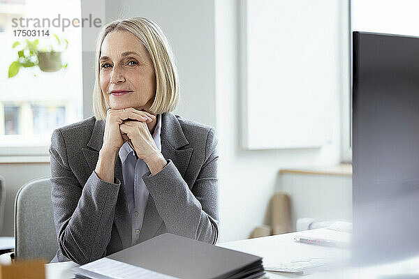 Blonde Geschäftsfrau mit den Händen am Kinn am Schreibtisch