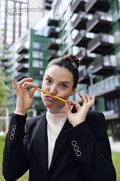 Geschäftsfrau macht Schnurrbart mit Bleistift auf gespitzten Lippen im Büropark