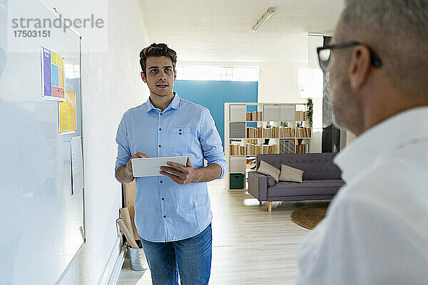 Kollege hält Tablet-PC in der Hand und diskutiert mit Geschäftsmann neben Whiteboard im Büro