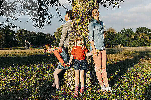 Familie hält Händchen und steht um Baum im Park