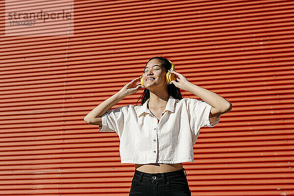 Lächelnde Frau  die vor einer Wellwandwand über Kopfhörer Musik hört