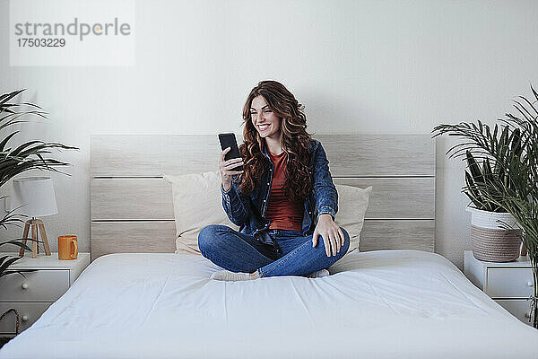 Lächelnde Frau benutzt Smartphone zu Hause im Bett