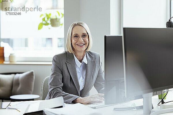 Lächelnde Geschäftsfrau sitzt am Schreibtisch im Büro