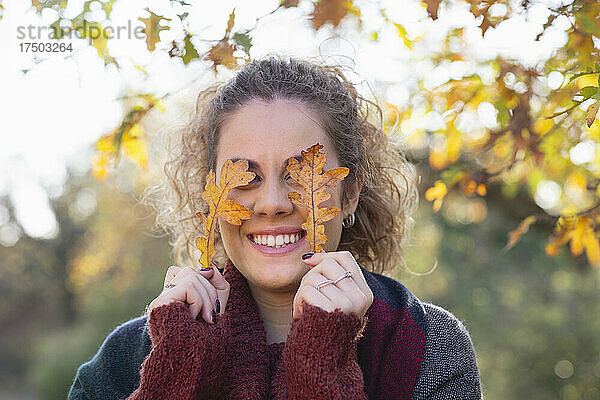 Lächelnde junge Frau hält Herbstblätter vor Augen im Wald