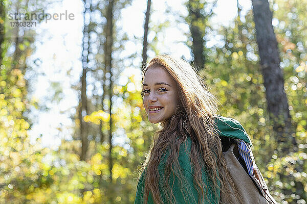 Lächelnde Frau mit Rucksack im Wald an einem sonnigen Tag
