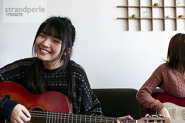 Lächelnde Frau  die zu Hause mit einer Freundin Gitarre spielt