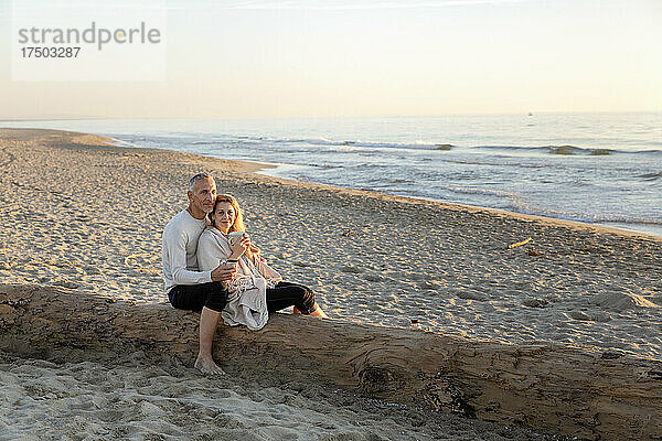 Frau mit Teebecher stützt sich auf Mann  der am Strand sitzt