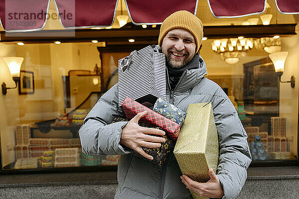 Lächelnder Mann hält Weihnachtsgeschenke vor dem Laden