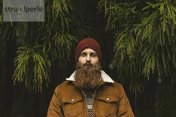 Junger Mann mit braunem Bart und Jacke im Wald