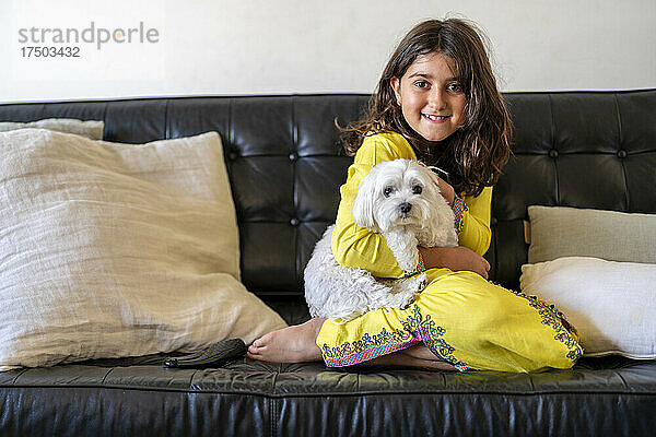 Lächelndes Mädchen sitzt mit Hund zu Hause auf dem Sofa