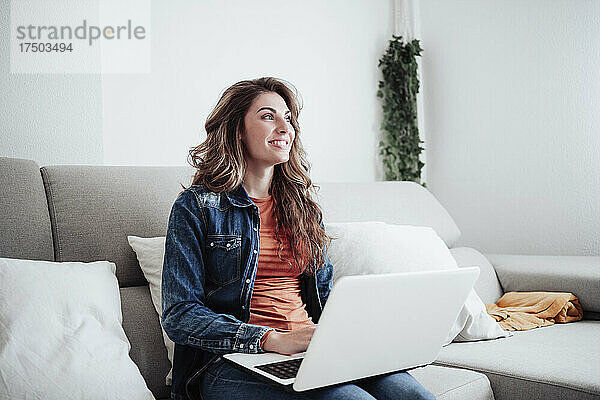 Lächelnde Frau mit Laptop  die zu Hause träumt
