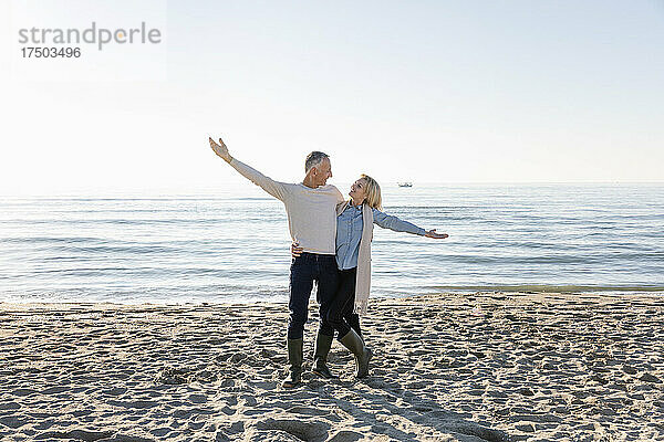 Paar mit ausgestrecktem Arm steht am Strand
