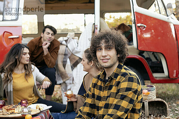 Lächelnder Mann mit Freunden  die sich beim Picknick vor dem Lieferwagen unterhalten