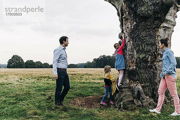 Eltern schauen ihren Töchtern beim Spielen auf einem Baum im Park zu