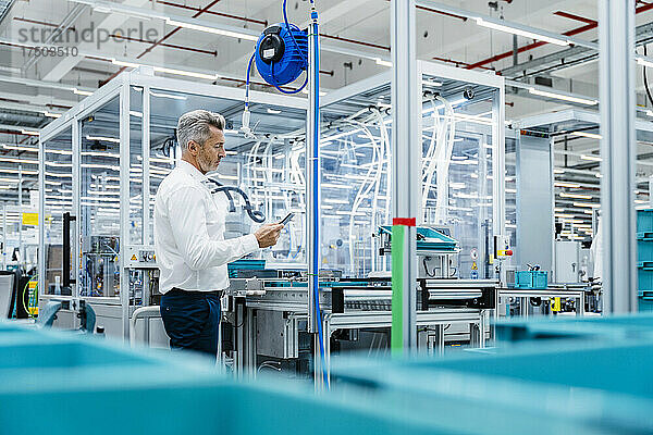 Geschäftsmann nutzt digitales Tablet am Fließband in der Fabrik
