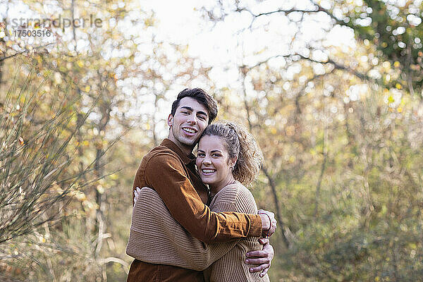 Lächelndes junges Paar  das sich im Herbstwald umarmt