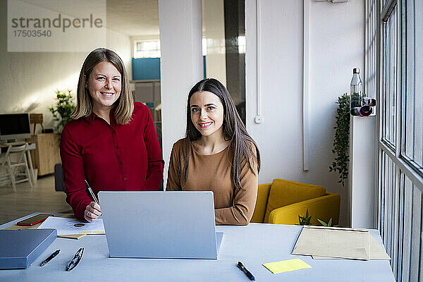 Lächelnde Geschäftsfrauen mit Laptop am Schreibtisch im Büro