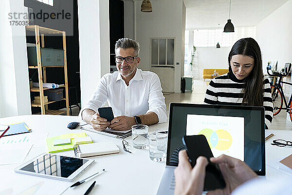 Geschäftsmann mit Smartphone sitzt mit Kollegen im Büro
