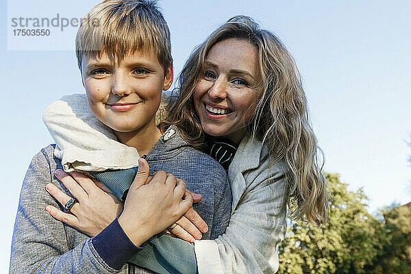 Glückliche blonde Frau umarmt Sohn im Park