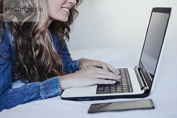 Lächelnde junge Frau benutzt Laptop im Schlafzimmer