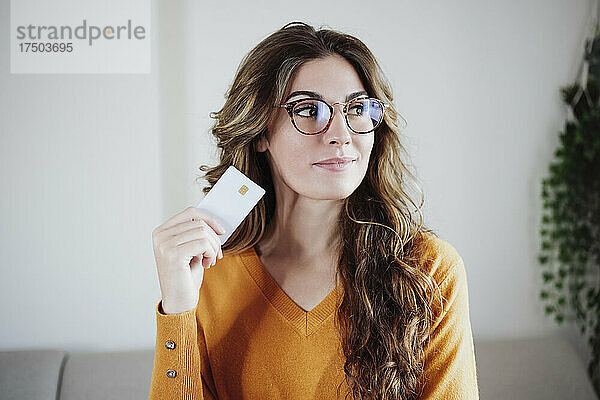 Schöne Frau mit Brille hält Kreditkarte zu Hause in der Hand