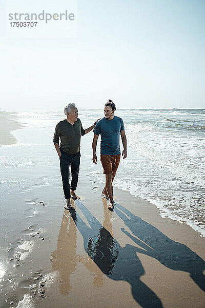 Vater geht mit Sohn an einem sonnigen Tag in der Nähe der Küste am Strand spazieren