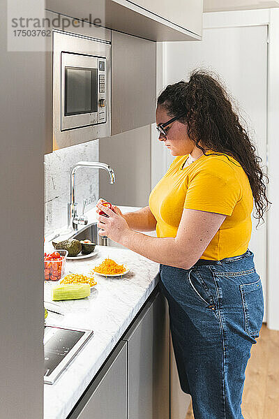 Junge Frau reibt Käse und steht zu Hause in der Küche