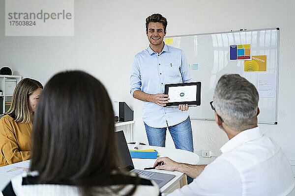 Junger Geschäftsmann zeigt seinen Kollegen im Büro eine Präsentation auf einem Tablet-PC