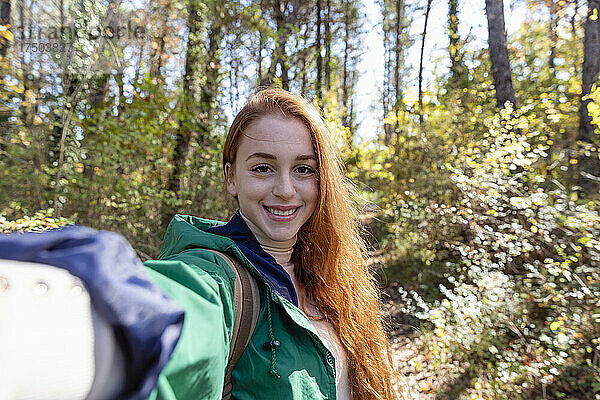 Lächelnde rothaarige junge Frau wandert im Wald
