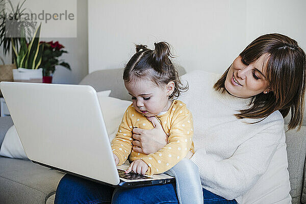 Lächelnde Mutter blickt Tochter mit Laptop auf Sofa an