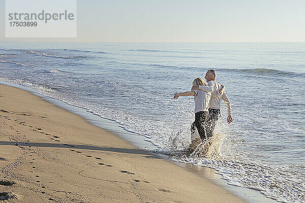 Paar bespritzt sich am Strand gegenseitig mit Wasser
