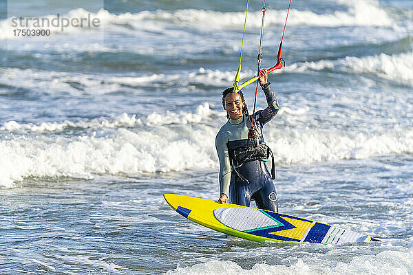 Glückliche Frau mit Kiteboard  die den Griff eines Drachenfallschirms im Wasser hält