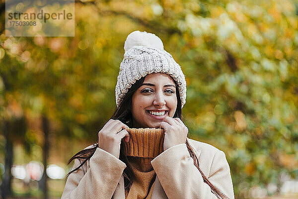 Lächelnde Frau mit Strickmütze und Pullover im Park