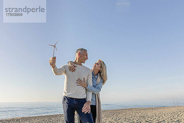Mann hält Windturbinenmodell und blickt Frau am Strand an