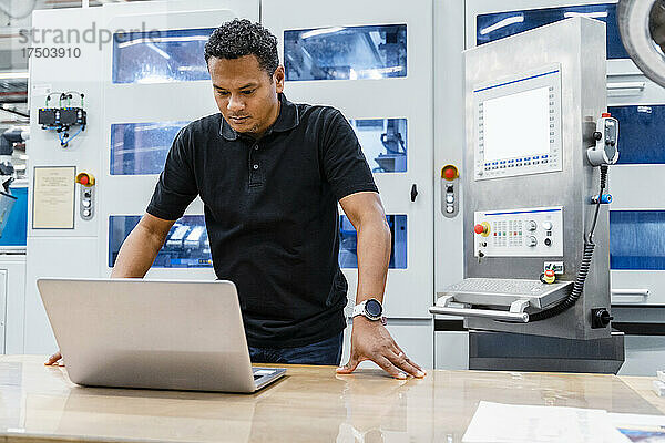 Wartungstechniker schaut in automatisierter Fabrik auf Laptop