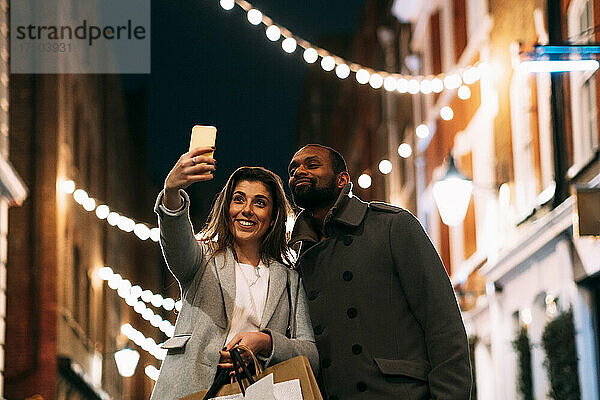 Lächelnde Frau macht nachts ein Selfie mit ihrem Freund per Smartphone