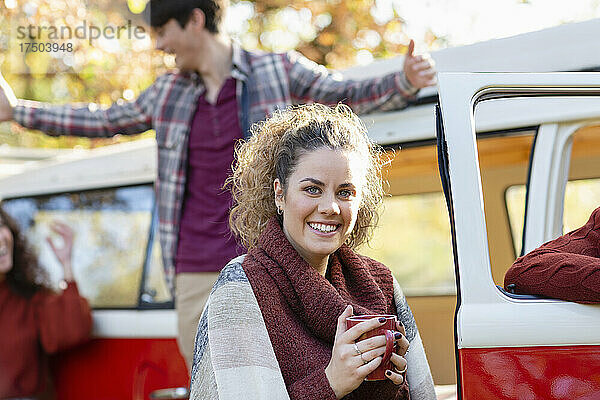 Lächelnde Frau trinkt Kaffee mit Freunden und hat am Wochenende Spaß im Hintergrund