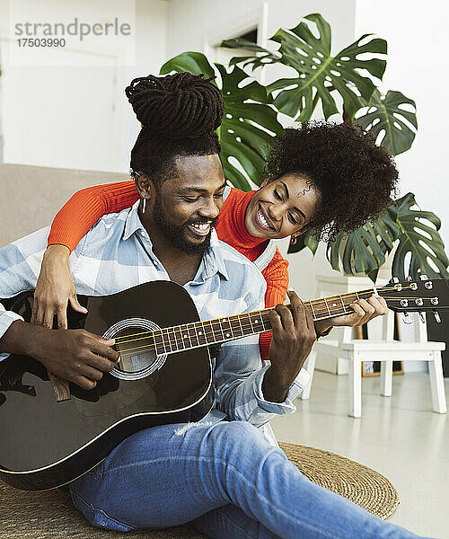 Lächelnde junge Frau lernt Gitarre von ihrem Freund