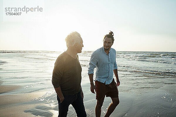 Vater und Sohn spazieren am Strand entlang der Küste