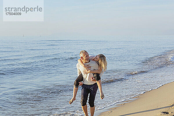 Mann huckepack  Frau am Strand