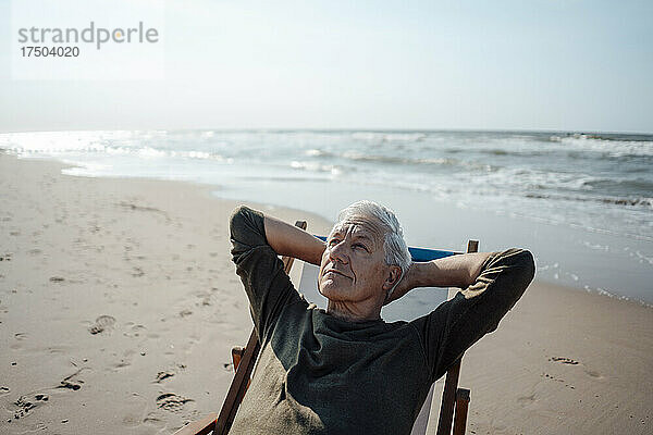 Älterer Mann schaut nach oben und entspannt sich auf einem Stuhl am Strand