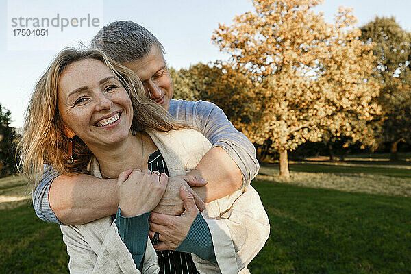 Mann umarmt lächelnde blonde Frau im Park