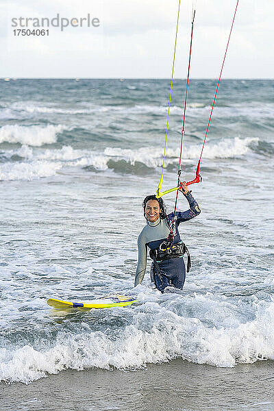 Lächelnde Frau mit Kiteboard  die den Griff eines Drachenfallschirms im Wasser hält