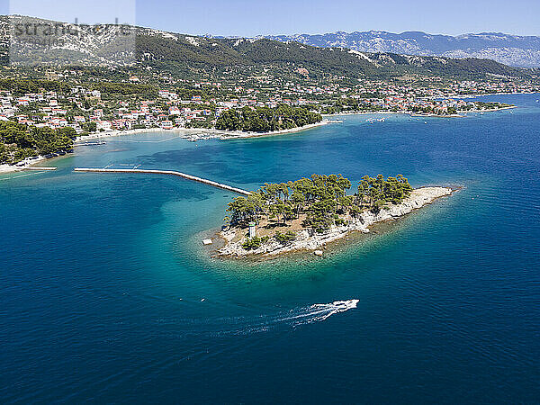 Kroatien  Gespanschaft Primorje-Gorski Kotar  Rab  Drohnenansicht eines Motorboots  das an einer kleinen Küsteninsel mit der Stadt im Hintergrund vorbeifährt
