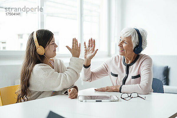 Mädchen mit Kopfhörern gibt der Großmutter zu Hause High-Five