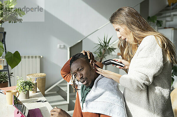 Schwangere Frau mit Haarschneider schneidet einem Mann zu Hause die Haare