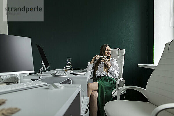 Geschäftsfrau sitzt mit Kaffeetasse im Büro